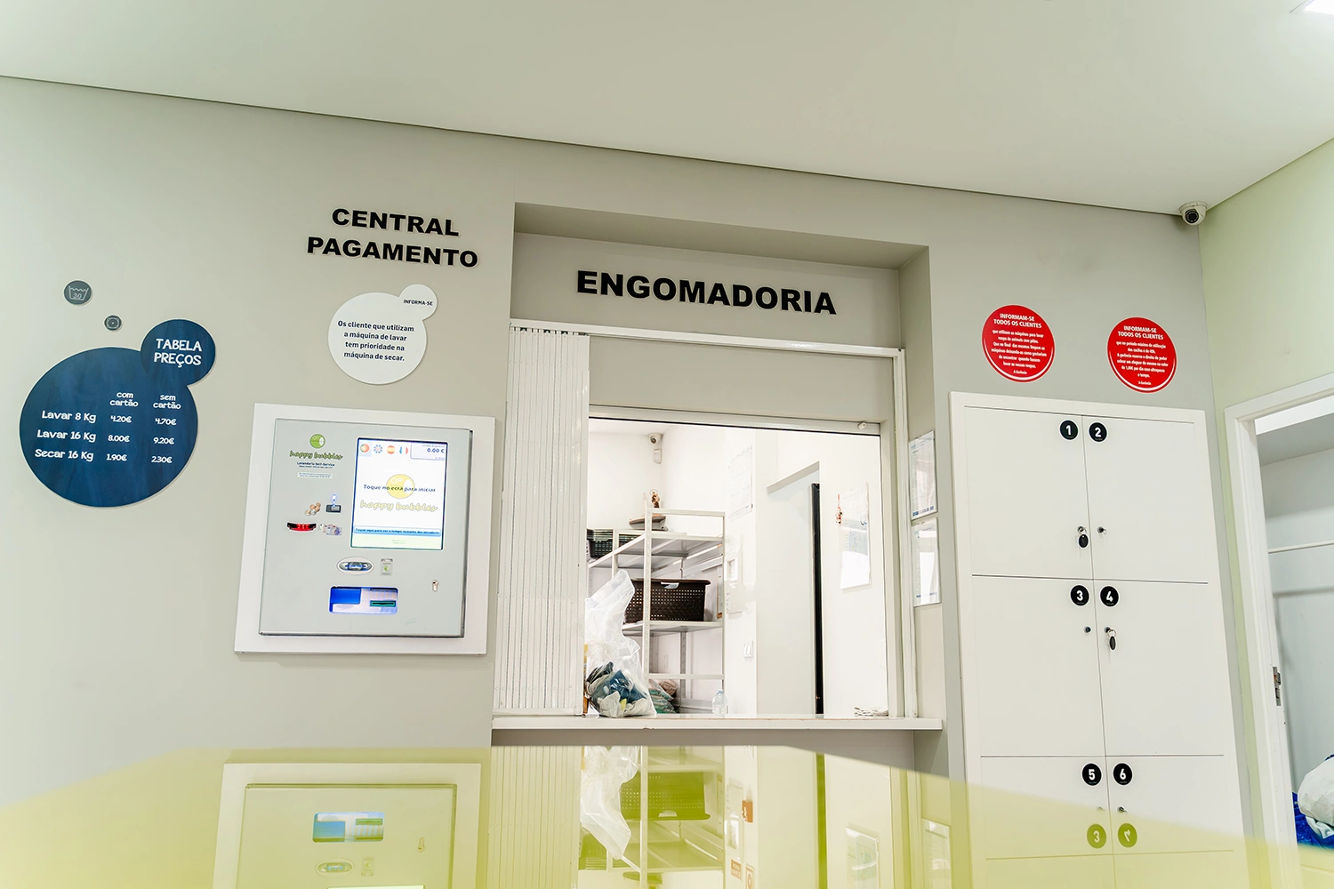 Vista da área de engomadoria com iluminação natural e máquinas self-service - ambiente profissional para cuidados têxteis